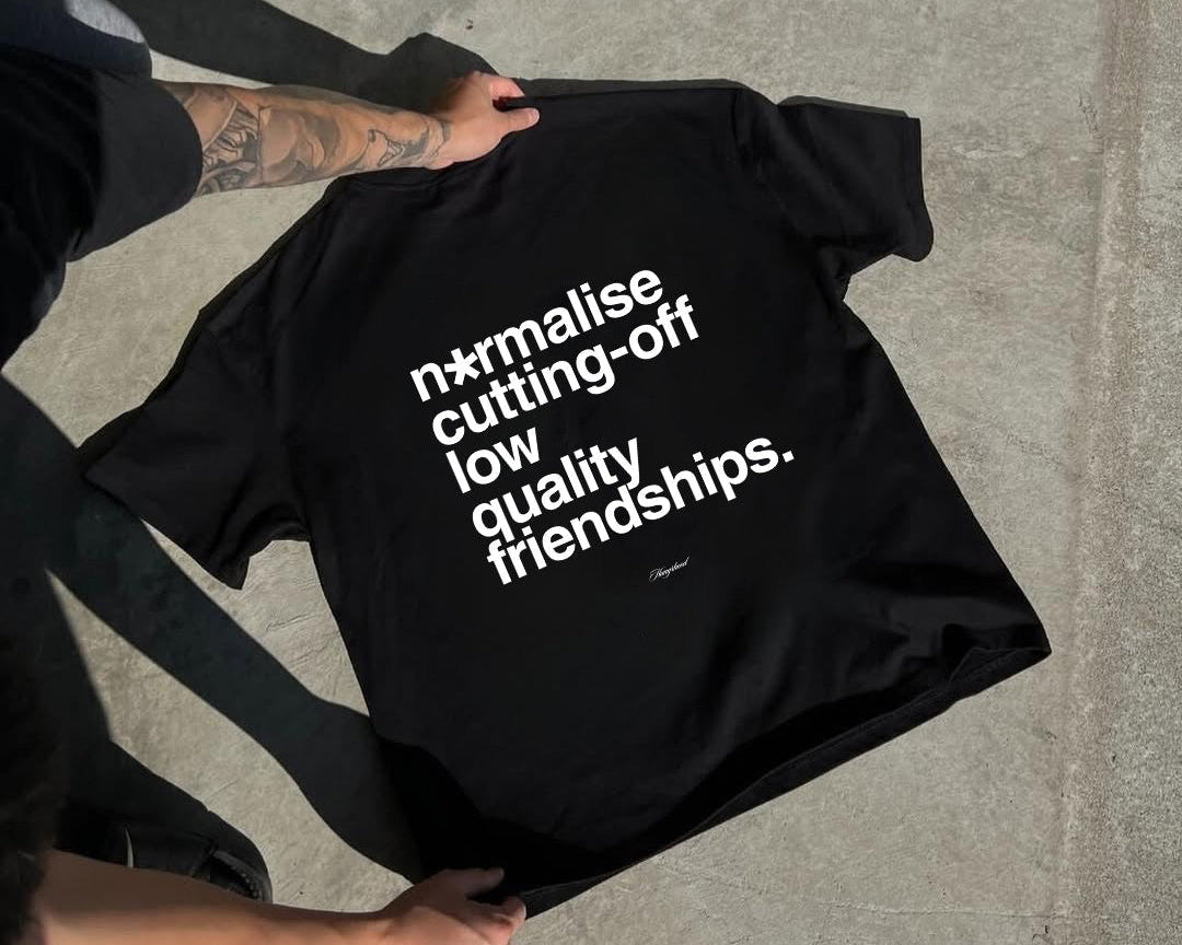 Black t-shirt with white text 'Normalise cutting off low quality friendships' on a concrete surface